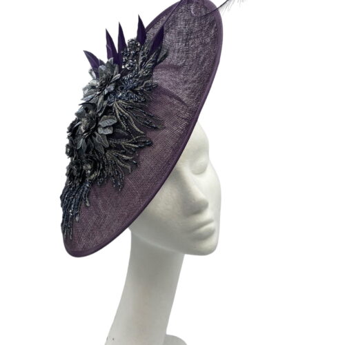 Purple saucer style headpiece with pewter embellishment to the side finished with a spray of colour matching feathers.